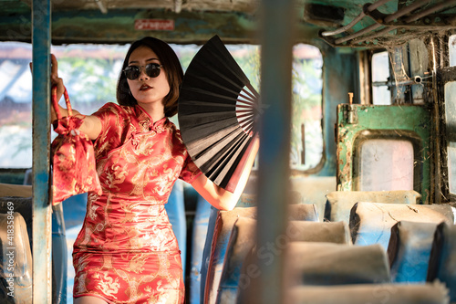 Photography Portrait beauty woman wear cheongsam with fan and holding bag of oranges in chinese new year on old dirty bus