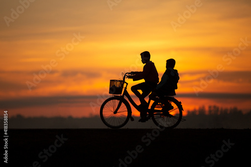 The boys riding the bicycle during the evening with the background of sunset in summer. Both child feeling happiness with his lifestle