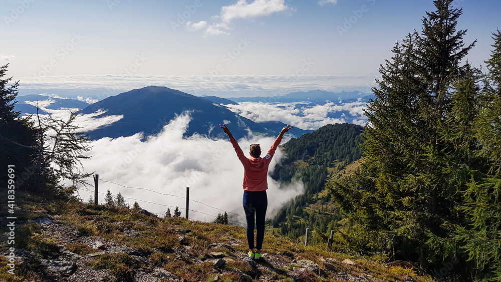 A woman enjoying the idyllic view on Alpine valley from the top of Granattor in Austrian Alps. The valley is shrouded in fog. The slopes are lush green. Many mountain poking above the clouds. Freedom A woman enjoying the idyllic view on Alpine valley from the top of Granattor in Austrian Alps. The valley is shrouded in fog. The slopes are lush green. Many mountain poking above the clouds. Freedom