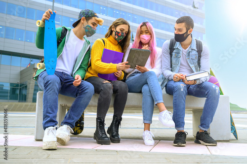 Group of students wearing face mask sitting on bench outside the campus studying together - New normal lifestyle concept with young people at school