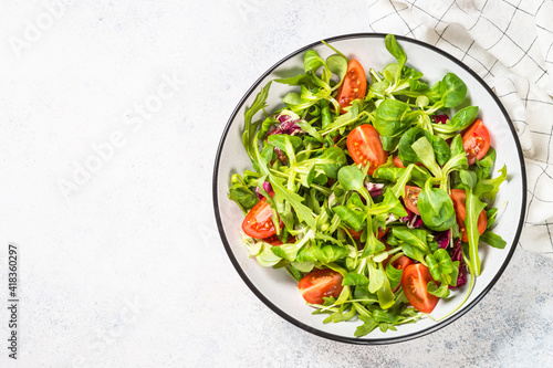 Green salad with arugula, lamb and tomatoes. Healthy vegan dish. Top view at white table.