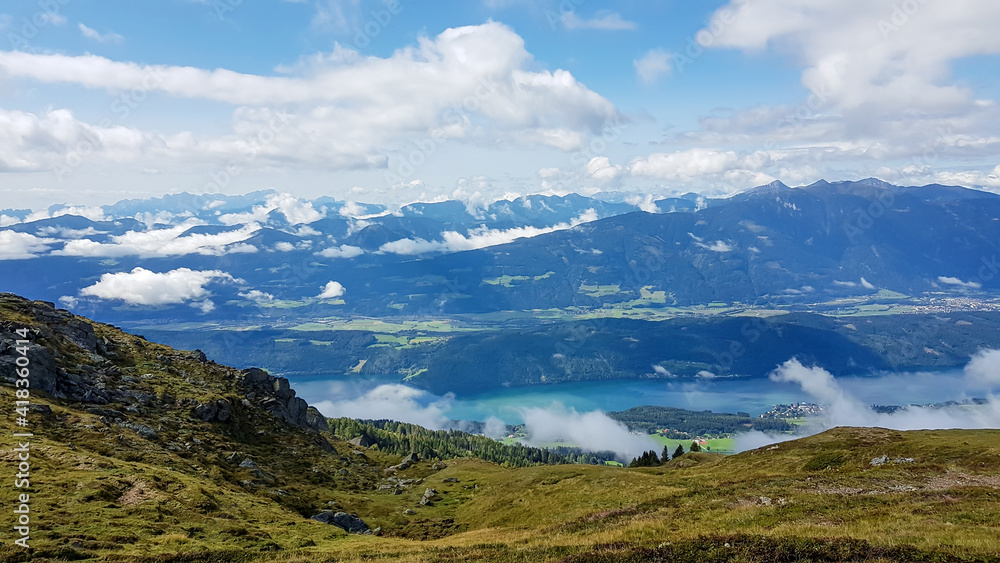 A panoramic view on the Millstaettersee from Granattor in Austrian Alps. The distant lake is surrounded by high mountains. There are few clouds above the lake and the valley. Endless mountain chains A panoramic view on the Millstaettersee from Granattor in Austrian Alps. The distant lake is surrounded by high mountains. There are few clouds above the lake and the valley. Endless mountain chains