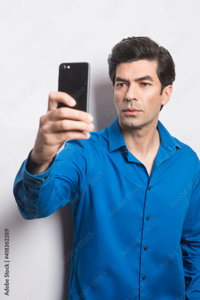 uomo moro in camicia blu fa una foto con il suo smartphone, isolato su sfondo su sfondo bianco