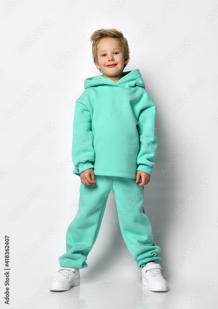 Happy teenager boy in blue turquoise sportswear posing on light background