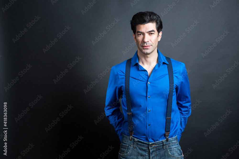 uomo moro in camicia blu e bretelle, isolato su sfondo nero