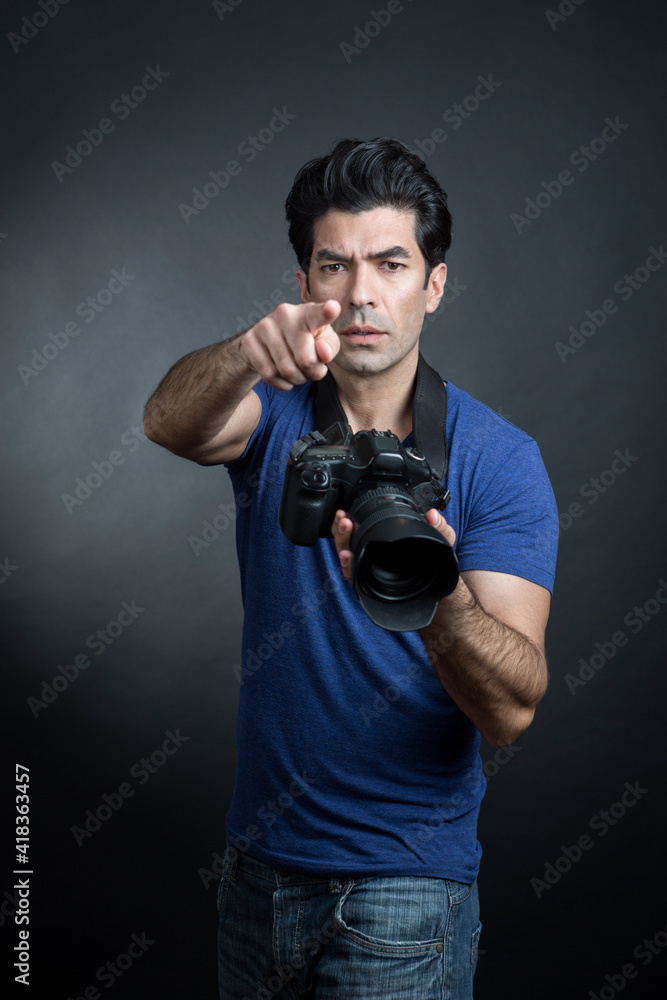 fotografo moro in maglietta blu e fotocamera al collo fa una foto e da delle indicazioni a qualcuno , isolato su sfondo nero