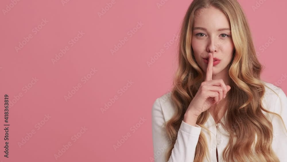 An attractive young woman is doing secret gesture standing isolated over pink wall in the studio An attractive young woman is doing secret gesture standing isolated over pink wall in the studio