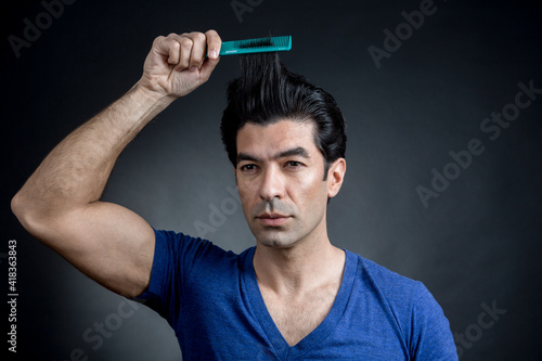 uomo moro in maglietta blu si pettina i capelli con espressione sicura di se, isolato su sfondo nero photo