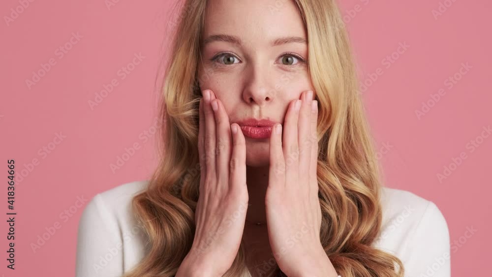 A happy surprised young blonde woman is looking to the camera standing isolated over a pink wall in the studio A happy surprised young blonde woman is looking to the camera standing isolated over a pink wall in the studio