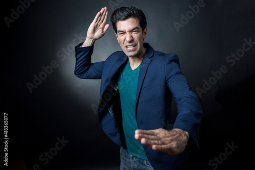 Uomo moro con maglia verde e giacca blu che si muove con colpi di karate, isolato su sfondo scuro photo