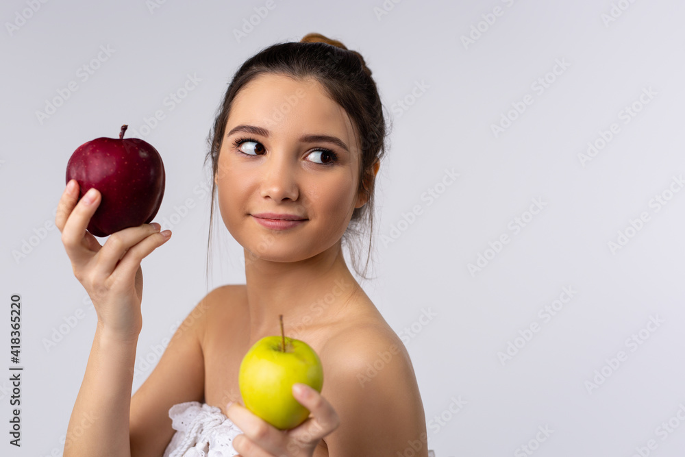 An attractive brunette wrapped in a white towel holds apples in her hands and looks to the side. Studio background. Side advertising space. An attractive brunette wrapped in a white towel holds apples in her hands and looks to the side. Studio background. Side advertising space.
