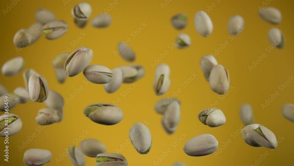 Close-up of salted pistachios flying up on a yellow background in slow motion Close-up of salted pistachios flying up on a yellow background in slow motion