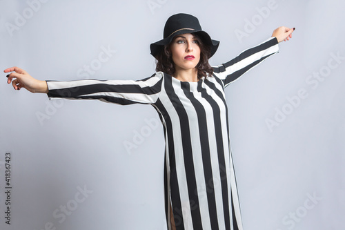 Donna con i capelli neri  vestita  con una maglia a righe e un cappello nero distende le braccia  , isolata su sfondo bianco photo