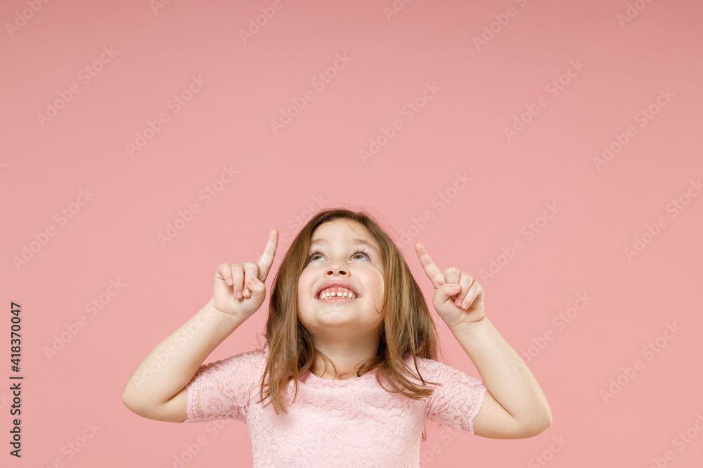 Little kid girl 5-6 years old in dress point fingers up on workspace commercial promo area mockup copyspace isolated on pastel pink background child studio portrait. Mother's Day love family concept.