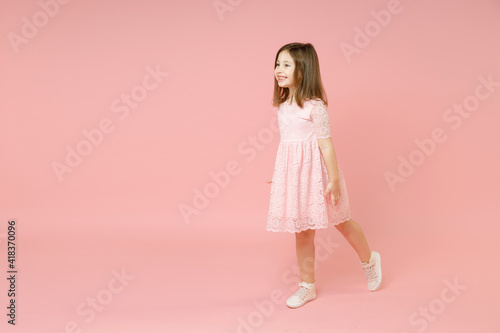 Full body length little cute kid girl 5-6 years old wears rosy dress have fun walk go step isolated on pastel pink background child studio portrait. Mother's Day love family people lifestyle concept.