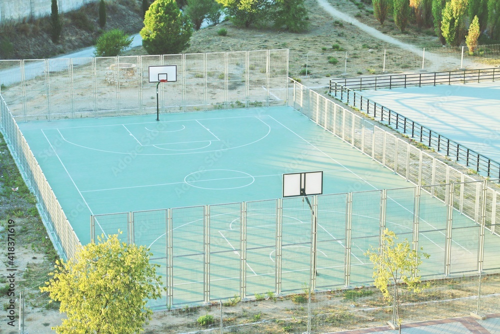 Fotografia do Stock: Cancha de baloncesto pública en el barrio residencial  de Montecarmelo, Madrid, España. Cancha de baloncesto verde junto a una  pista de patinaje sobre ruedas con los últimos rayos del