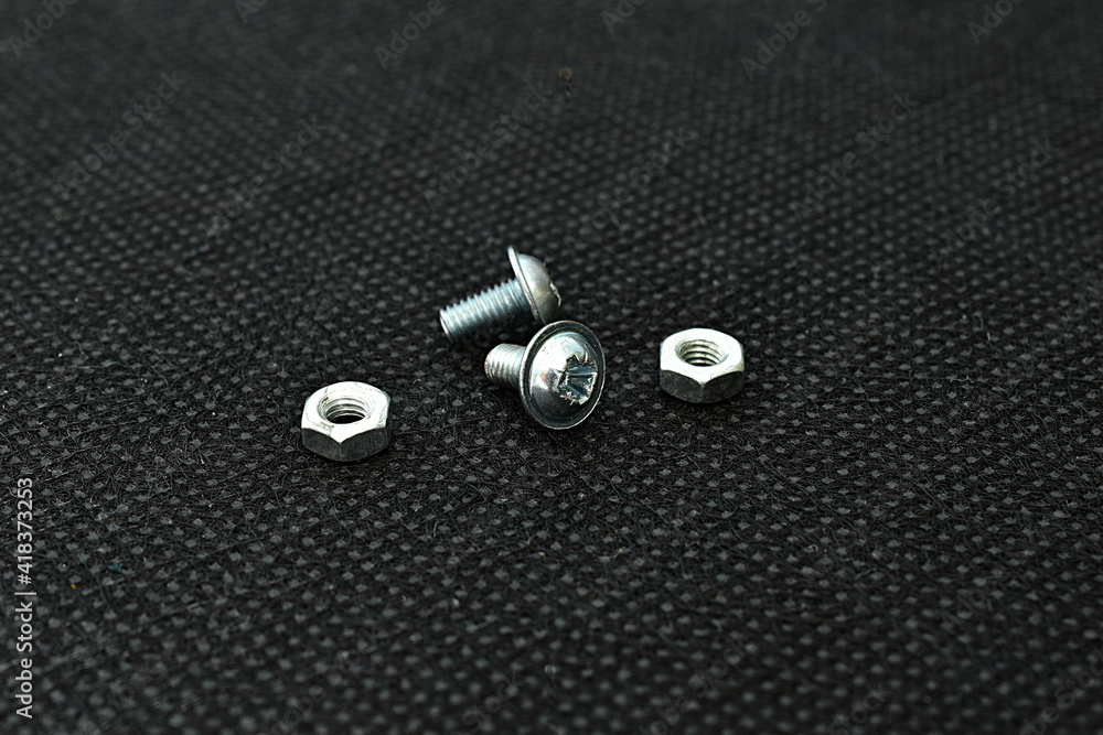 On the dark surface of the table there are two small bolts and two nuts. On the dark surface of the table there are two small bolts and two nuts.