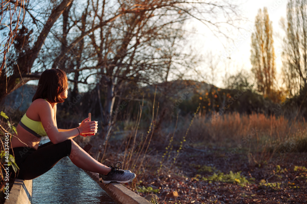 Young sporty woman eating healthy lunch in the field at the sunset