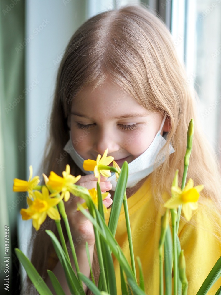 Coronavirus is over. Little girl sitting on the windowsill and removing face medical mask, sniffing yellow daffodil flowers. Take off the mask. Quarantine is over. Hello spring Coronavirus is over. Little girl sitting on the windowsill and removing face medical mask, sniffing yellow daffodil flowers. Take off the mask. Quarantine is over. Hello spring
