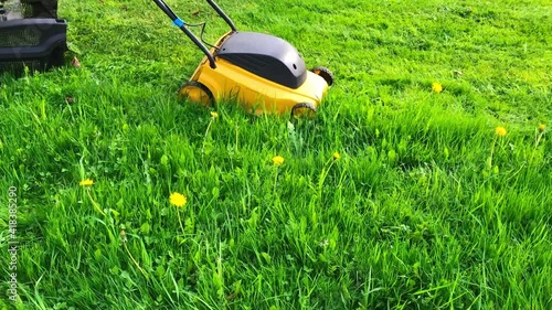 Yellow Electric lawn mower breaks down while mowing grass in garden. Breakdown of garden equipment