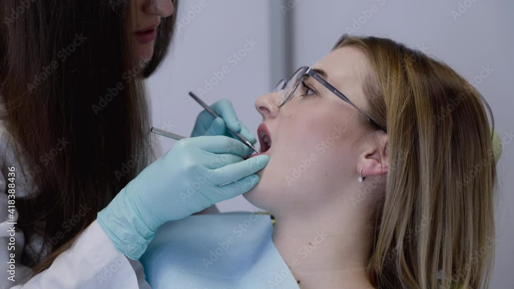 Female dentist in medical gloves scaling with tools patient's teeth in clinic Female dentist in medical gloves scaling with tools patient's teeth in clinic