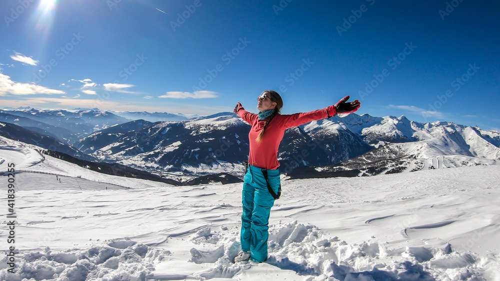 A young woman in colorful skiing outfit doing yoga at the top of Katschberg, ski resort in Austria. The woman spreads open her arms. Yogi's remedy. Solitude and awareness. Winter wonderland