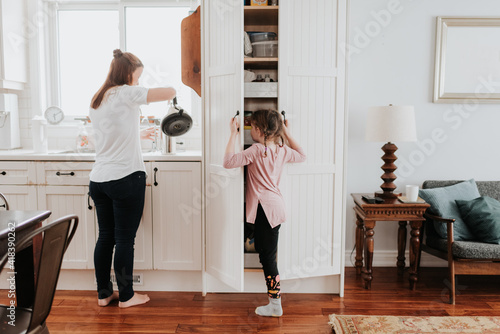 Mother pouring hot water, girl looking into cabinet in kitchen