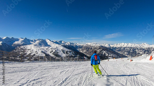 A man in colorful outfit skiing on the slopes of Katschberg in Austria. Panoramic view on the surrounding mountains. Winter wonderland. Sunny winter day. Perfectly groomed slopes. Happiness