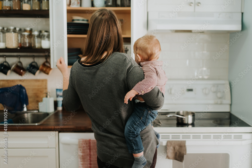Mother carrying baby son preparing food in kitchen, rear view Mother carrying baby son preparing food in kitchen, rear view