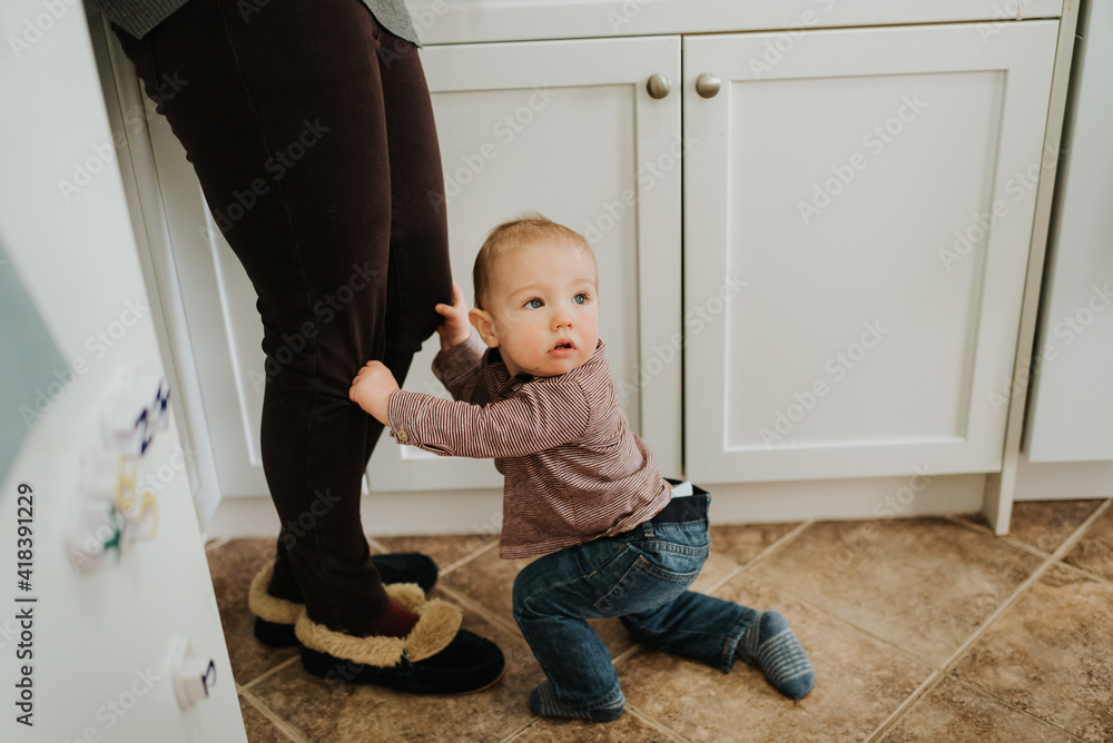 Baby boy in kitchen holding on to mother's legs Baby boy in kitchen holding on to mother's legs