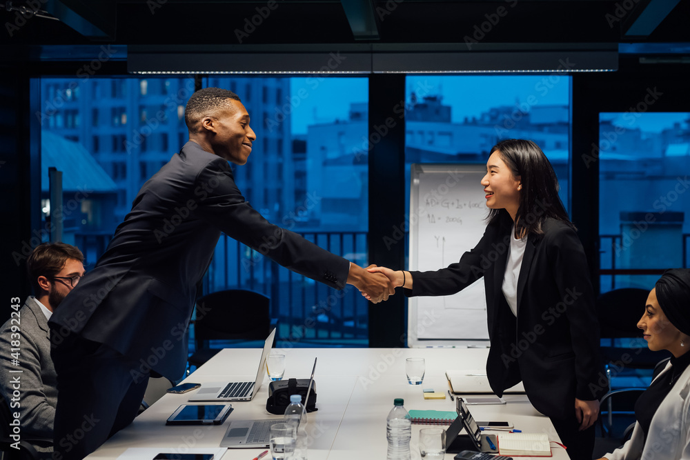 Businesswoman and male client shaking hands over conference table meeting