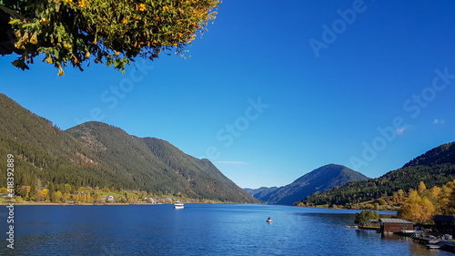 An idyllic view on the Weissensee lake surrounded by the Austrian Alps. The surface of the lake is calm and reflecting the mountains. Joyfulness and happiness. A tree crown in the upper corner photo