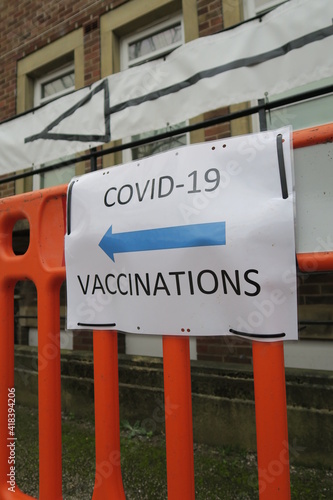 Covid-19 Vaccination signs to Vaccination clinic this way with blue arrow. Homemade signage found in the UK suburbs, DIY notice tells public which way to go for help during the coronavirus pandemic 