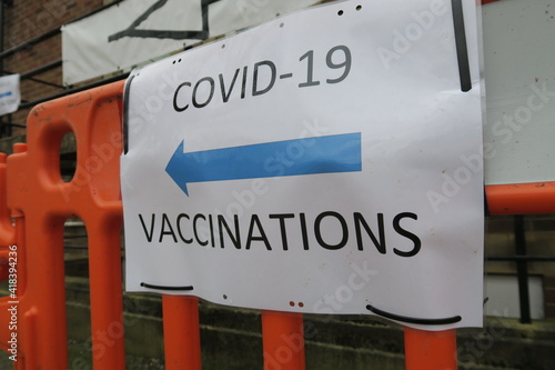 Covid-19 Vaccination signs to Vaccination clinic this way with blue arrow. Homemade signage found in the UK suburbs, DIY notice tells public which way to go for help during the coronavirus pandemic 