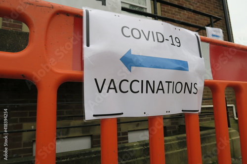Covid-19 Vaccination signs to Vaccination clinic this way with blue arrow. Homemade signage found in the UK suburbs, DIY notice tells public which way to go for help during the coronavirus pandemic 