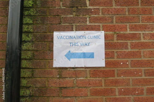 Covid-19 Vaccination signs to Vaccination clinic this way with blue arrow. Homemade signage found in the UK suburbs, DIY notice tells public which way to go for help during the coronavirus pandemic 
