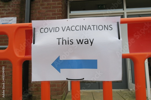 Covid-19 Vaccination signs to Vaccination clinic this way with blue arrow. Homemade signage found in the UK suburbs, DIY notice tells public which way to go for help during the coronavirus pandemic 