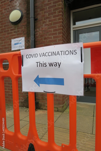 Covid-19 Vaccination signs to Vaccination clinic this way with blue arrow. Homemade signage found in the UK suburbs, DIY notice tells public which way to go for help during the coronavirus pandemic 