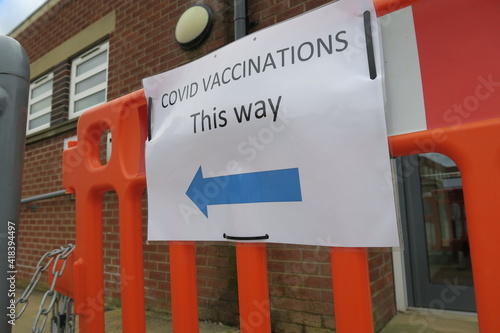 Covid-19 Vaccination signs to Vaccination clinic this way with blue arrow. Homemade signage found in the UK suburbs, DIY notice tells public which way to go for help during the coronavirus pandemic 