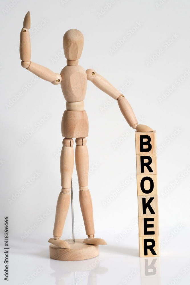 The wooden man raised his hand, and under his left hand he has cubes with the inscription - BROKER The wooden man raised his hand, and under his left hand he has cubes with the inscription - BROKER
