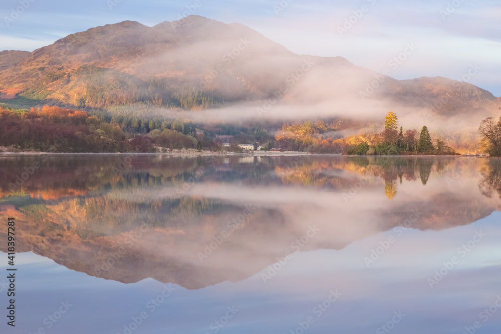 A calm tranquil mountain landscape reflection with morning mist on Loch Achray at Loch Lomond & The Trossachs National Park in the Scottish Highlands, Scotland.