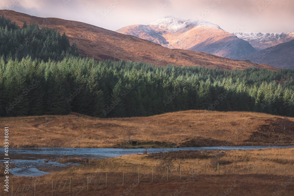 Golden sunlight on a snowcapped mountain and pine forest countryside landscape along the River Orchy in the Scottish Highlands outside of Tyndrum, Scotland. Golden sunlight on a snowcapped mountain and pine forest countryside landscape along the River Orchy in the Scottish Highlands outside of Tyndrum, Scotland.
