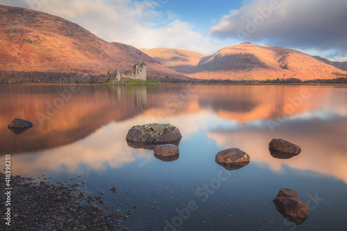 Scottish Highlands landscape of the historic ruins of Kilchurn Castle reflected on a calm, peaceful Loch Awe with sunset or sunrise golden light. photo