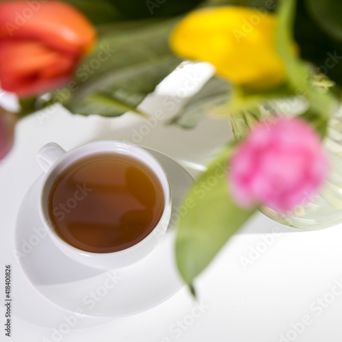 A bouquet of multi-colored tulips in a transparent vase and cup of tea