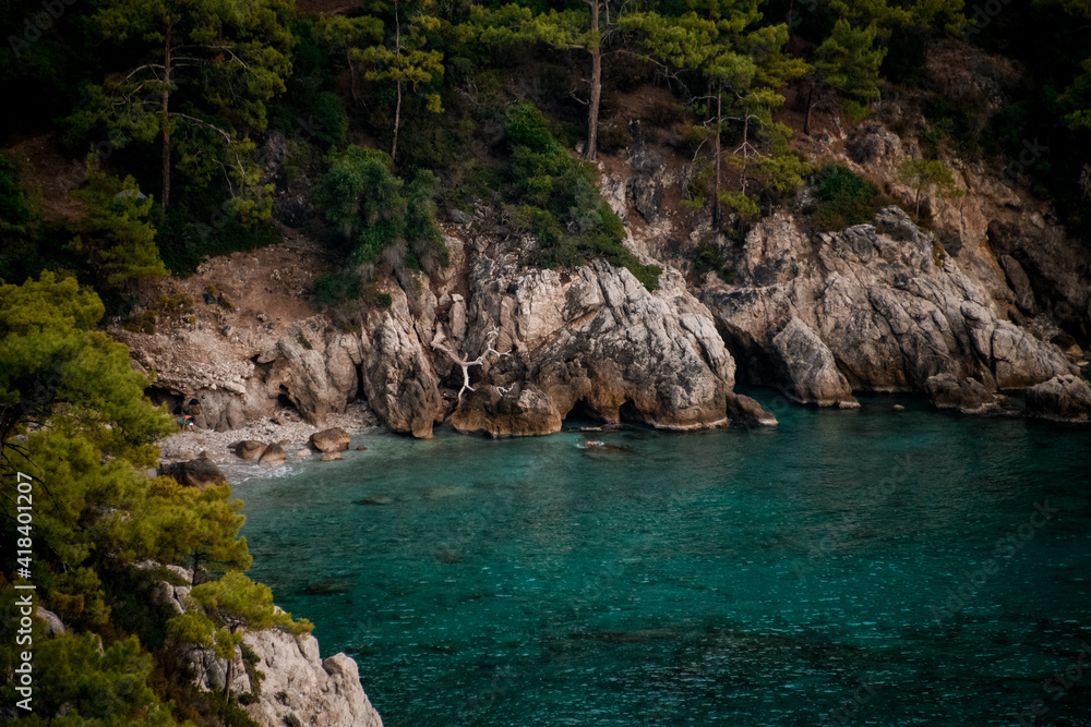 amazing view of rocky cliff with green pine trees and turquoise colored water.