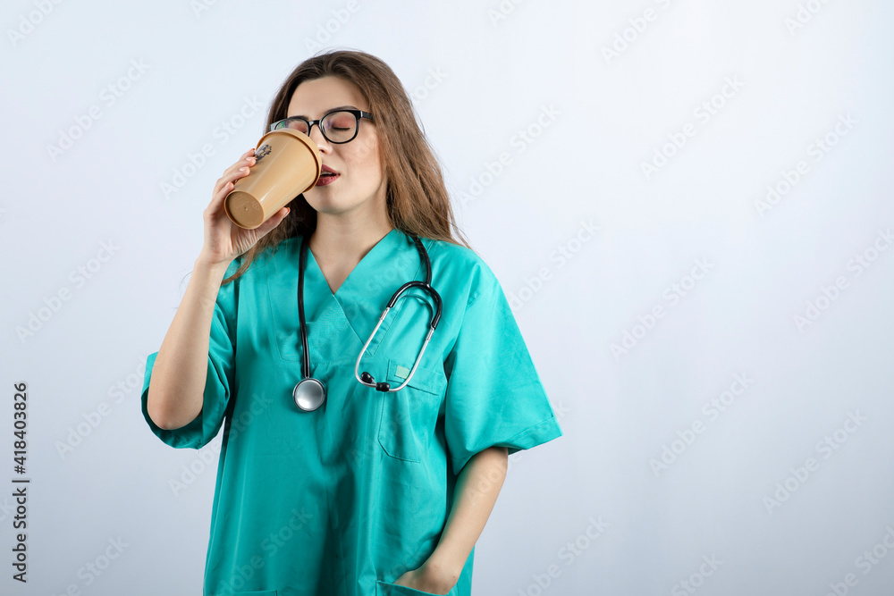 Young attractive nurse with stethoscope drinking from a cup of coffee Young attractive nurse with stethoscope drinking from a cup of coffee