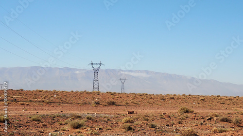 Energy tower and power line in desert landscape. Arid environment, hills in background and blue sky. 
