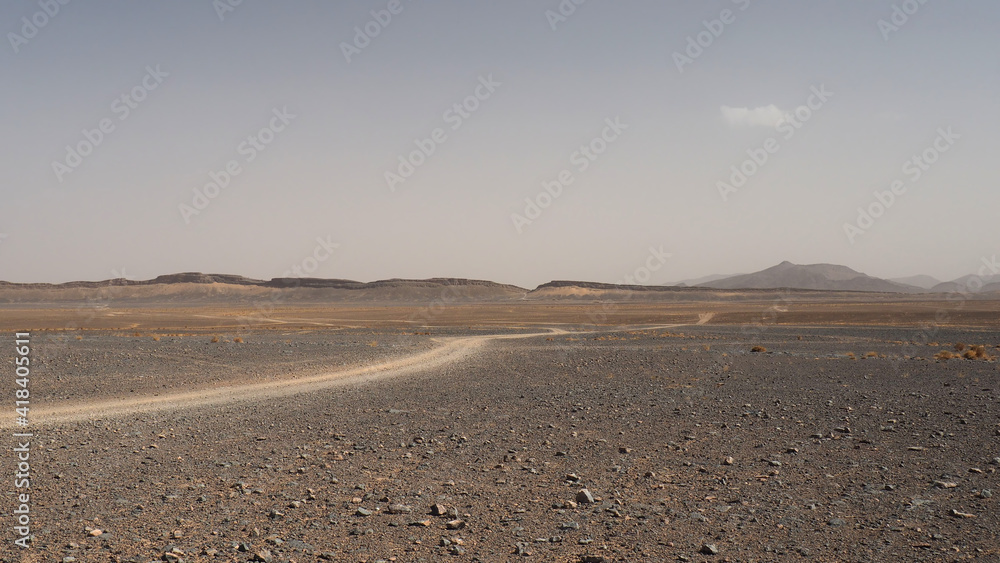 Desert plain landscape with car trail. Landscape of rocky desert with 4x4 car trail. Grey gravel, yellow sand, plain horizon with low hills and clear sky.