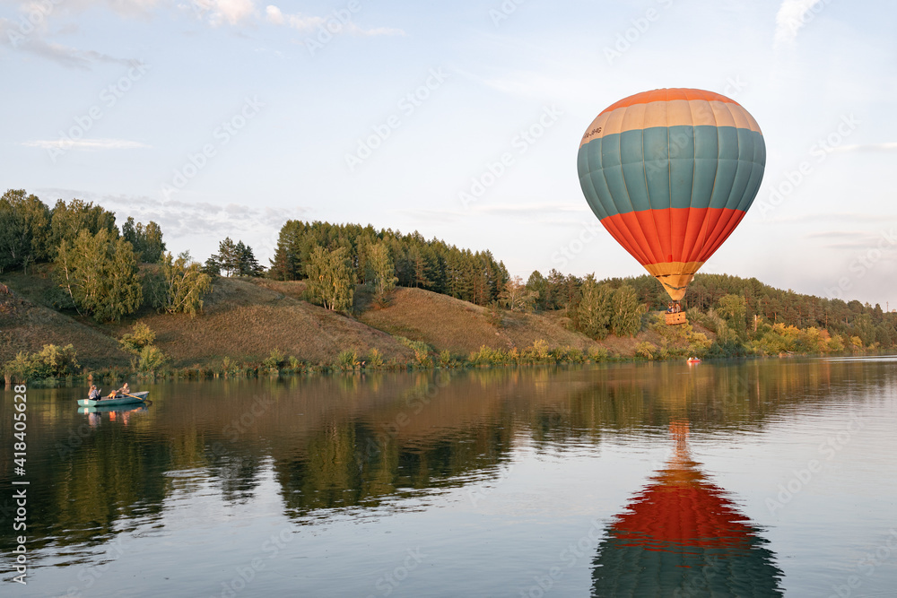 a balloon with people in a basket hovers over the hilly terrain above the water