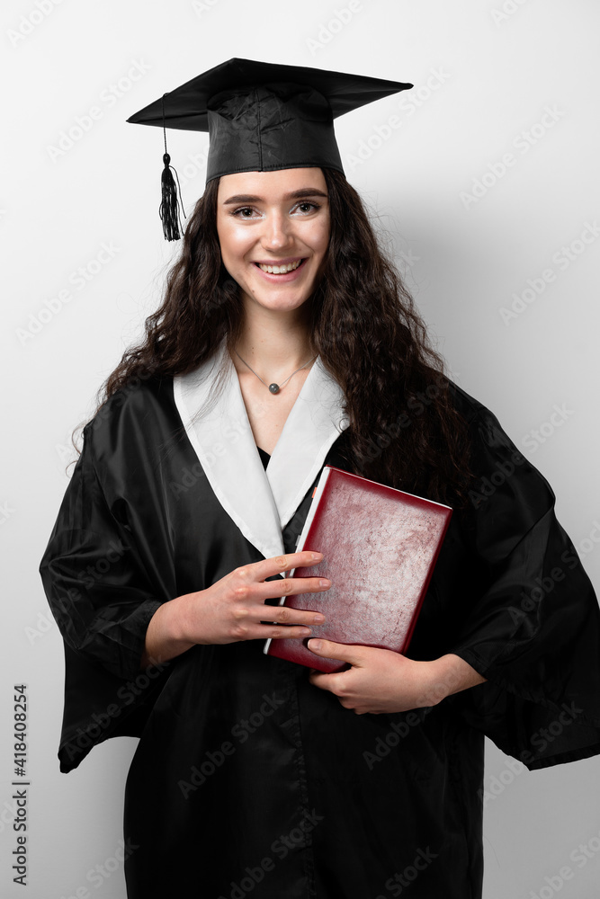 Student with book in graduation robe and cap ready to finish college. Future leader of science. Academician young woman in black gown smiling. Student with book in graduation robe and cap ready to finish college. Future leader of science. Academician young woman in black gown smiling.